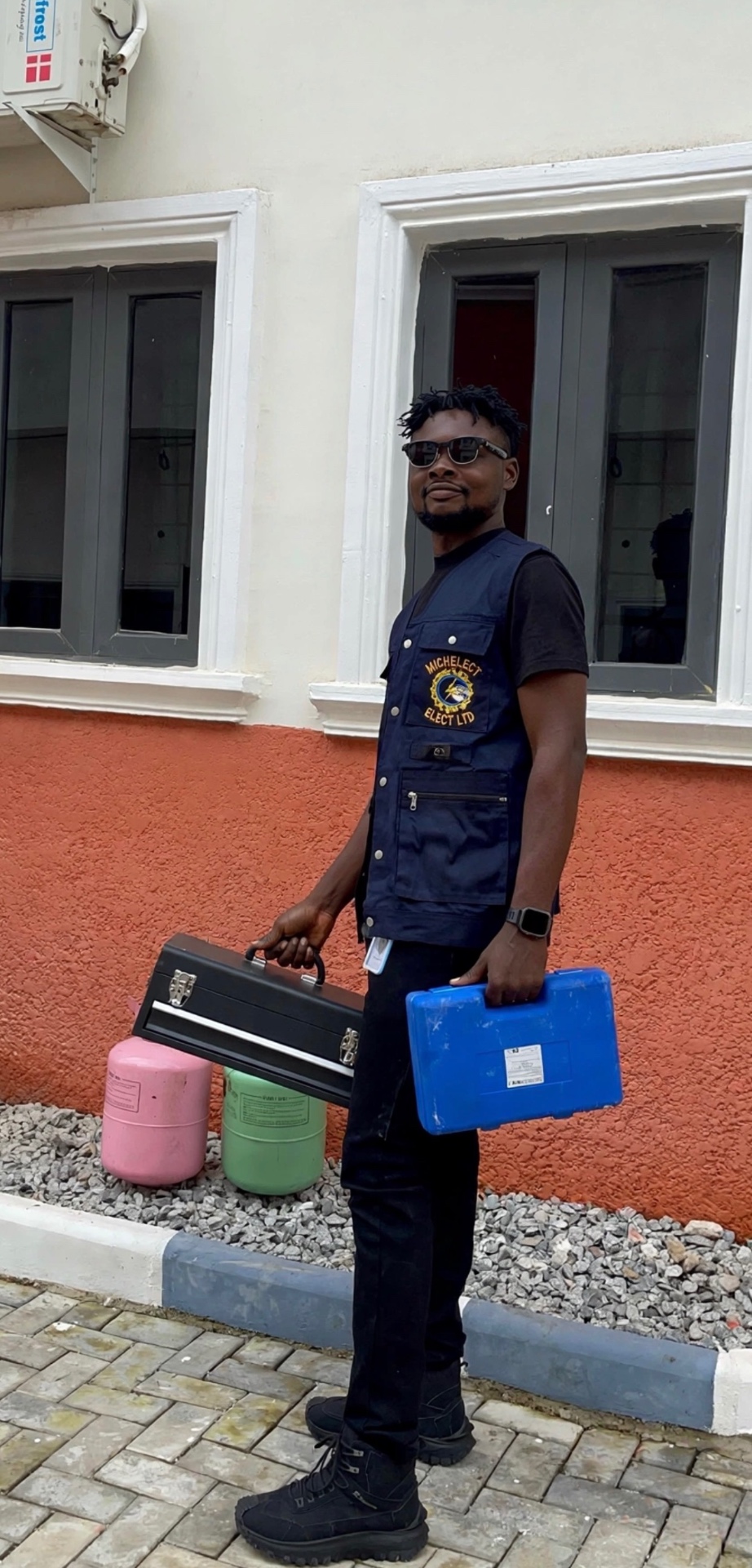 REE engineer in a MICHELECT ELECT LTD work vest holding electrical tool cases, full body